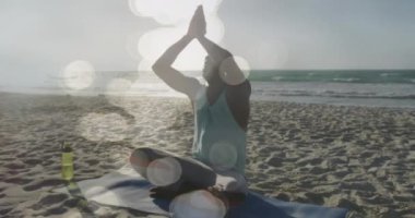 Sahilde yoga meditasyonu yapan Afro-Amerikan bir adam üzerinde parlayan ışıkların animasyonu. Küresel bağlantılar, refah, zindelik ve dijital olarak üretilen sağlıklı yaşam tarzı konsepti.