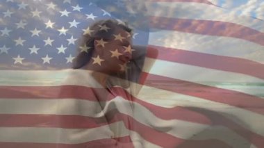 Amerikan bayrağının sahilde yürürken soğuk hisseden yaşlı beyaz bir kadının üzerinde dalgalanması. Dijital kompozit, çoklu pozlama, emeklilik, tatil, özgürlük ve vatanseverlik kavramı.