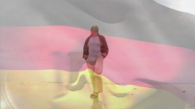 Alman bayrağının animasyonu, kıdemli beyaz adamın kumsalda cebinde yürümesi üzerine. Dijital kompozit, çoklu pozlama, emeklilik, tatil, özgürlük ve vatanseverlik kavramı.
