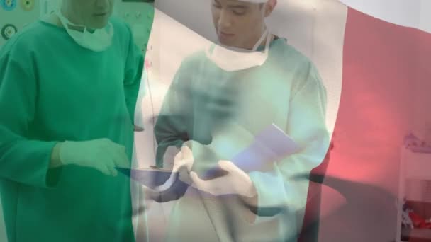 在手术室讨论病人报告时 意大利国旗在不同的外科医生之间摇曳的动画 数字合成 多重曝光 医疗保健 自由和爱国主义概念 — 图库视频影像
