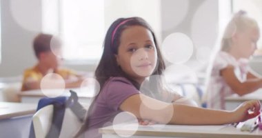 Sınıfta oturan mutlu melez liseli kız yerine bokeh ışıklı noktaların animasyonu. Okul, eğitim, çocukluk ve öğrenme, dijital olarak oluşturulan video.
