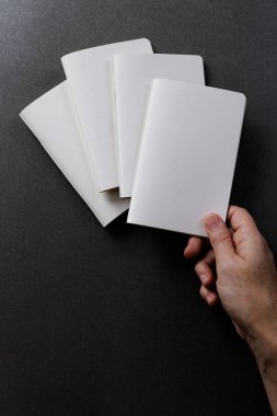 Siyah arka planda kopya alanı olan diğer defterlerin üzerinde bir defter tutan beyaz kadın eli. Edebiyat, okuma, boş zaman ve kitaplar..
