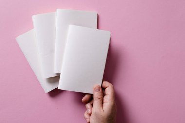 Pembe arka planda fotokopi alanı olan diğer defterlerin üzerinde bir defter tutan beyaz kadın eli. Edebiyat, okuma, boş zaman ve kitaplar..