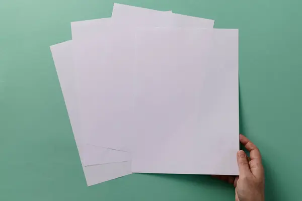 緑の背景にコピースペースで紙の上に紙の作品を保持している白人女性の手 — ストック写真