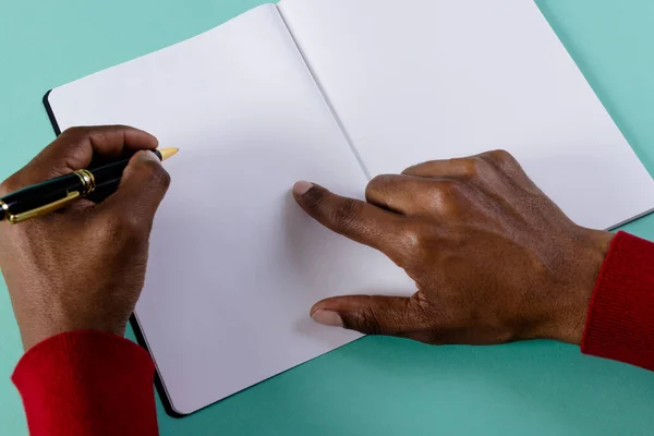 stock image Hands of biracial man holding pen, writing in notebook with copy space on green background. Literature, writing, leisure time and books.