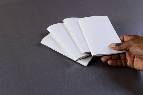 Hand of biracial man holding notebook over notebooks with copy space on grey background. Literature, reading, leisure time and books.