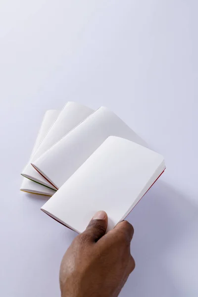 Hand of biracial man holding notebook over notebooks with copy space on white background. Literature, reading, leisure time and books.
