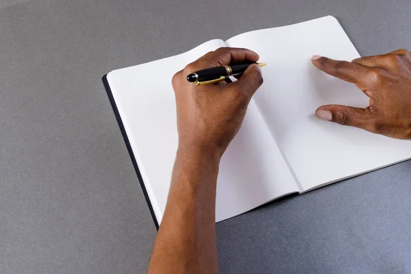 Hands of biracial man holding pen and writing in notebook with copy space on grey background. Literature, writing, leisure time and books.