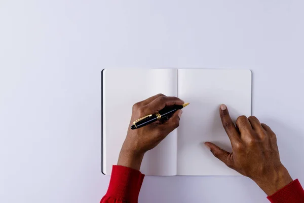 Hands of biracial man holding pen, writing in notebook with copy space on white background. Literature, writing, leisure time and books.