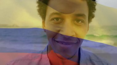 Kolombiya bayrağının hareketlendirilmesi, gülümseyen Afro-Amerikan bir adamın denize karşı duruşu. Dijital kompozit, çoklu pozlama, tatil, plaj, özgürlük, gurur ve vatanseverlik kavramı.
