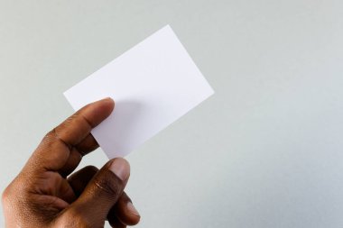 Beyaz arka planda fotokopi alanı olan beyaz kartvizit tutan melez bir adamın eli. İş, kartvizit, kırtasiye ve yazma alanı kavramı.