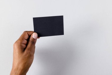 Beyaz arka planda fotokopi alanı olan siyah kartvizit tutan melez bir adamın eli. İş, kartvizit, kırtasiye ve yazma alanı kavramı.