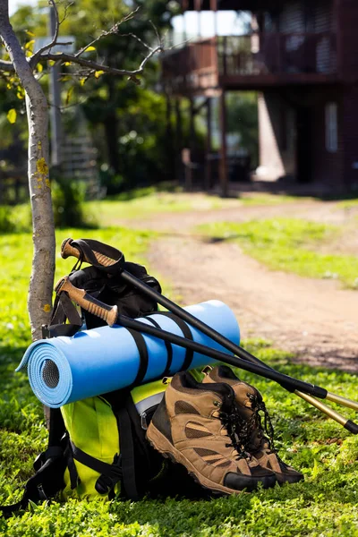 Vertical image of hiking poles, shoes and backpack with mat over log cabin on sunny day. Nature, agriculture, summer, hiking and rural landscape.