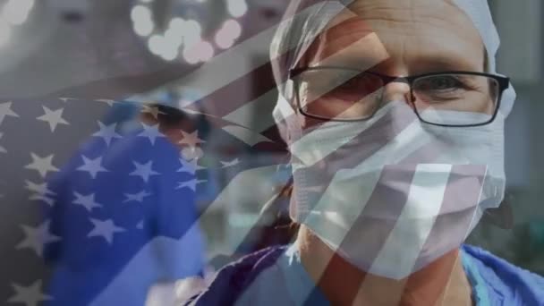 医院内身穿外科口罩的高加索男外科医生的肖像上飘扬着美国国旗 医疗和爱国主义概念 — 图库视频影像