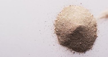 Video of close up of sand grains pouring into heap and copy space on white background. Sand, texture and pattern concept.
