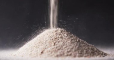 Video of close up of sand grains pouring into heap and copy space on black background. Sand, texture and pattern concept.