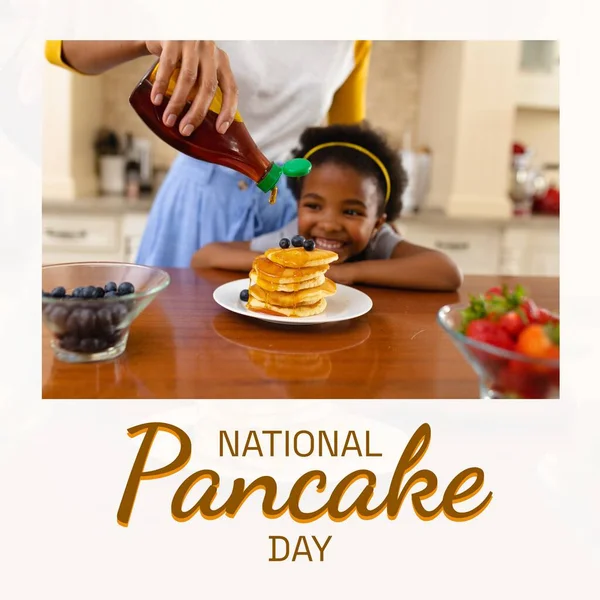 National pancake day text and happy african american daughter with mother pouring syrup on pancakes. American pancake day tradition and food celebration campaign digitally generated image.