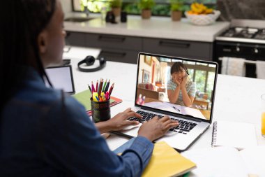 Afro-Amerikalı genç kız evde bilgisayardan arkadaşlarıyla ev ödevlerini tartışıyor. Değiştirilmemiş, birlikte, teknoloji, eğitim, öğrenci, e-öğrenme, çevrimiçi, ekran ve ev kavramı.