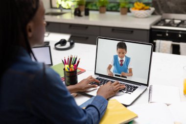 Bilgisayarda çalışırken video üzerinden arkadaşlarıyla konuşan Afrikalı Amerikalı bir genç. Değiştirilmemiş, arkadaşlar, çocukluk, teknoloji, eğitim, öğrenci, e-öğrenme, ekran ve ev.