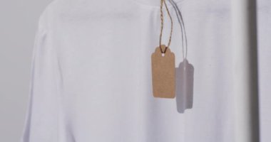 Gri arkaplanda etiketli beyaz tişört videosu ve kopyalama alanı. Moda, trendler ve giyim konsepti.