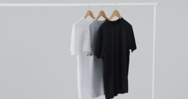 Askılarda beyaz, gri, siyah tişörtler ve beyaz arka planda fotokopi alanı. Moda, trendler ve giyim konsepti.