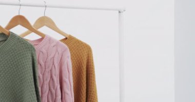 Askılarda üç renkli süveter ve beyaz arka planda fotokopi alanı. Moda, trendler ve giyim konsepti.