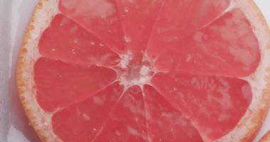 Kırmızı greyfurt dilimine düşen su damlalarının videosu. Beyaz arkaplanda kopyalama alanı var. Meyve ve tazeliği kavramı.