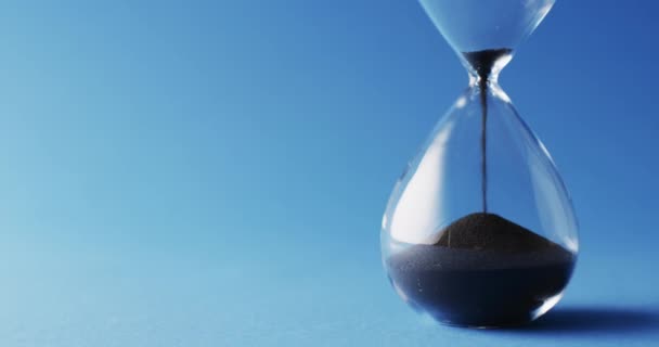Video Close Hourglass Black Sand Pouring Copy Space Blue Background — стокове відео