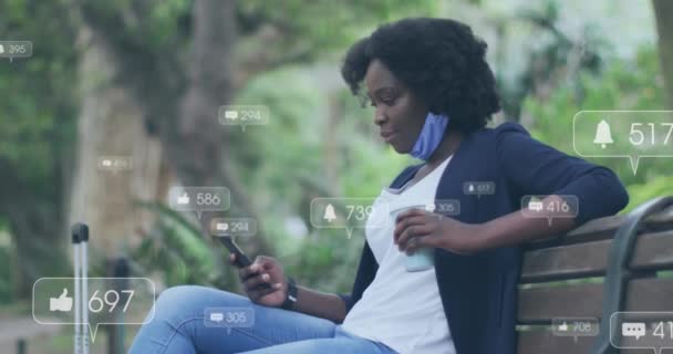 ベンチに座っているスマートフォンを使用してアフリカ系アメリカ人女性に対するソーシャルメディアアイコンのアニメーション ソーシャルメディアネットワーキングとコビド 19パンデミックコンセプト — ストック動画