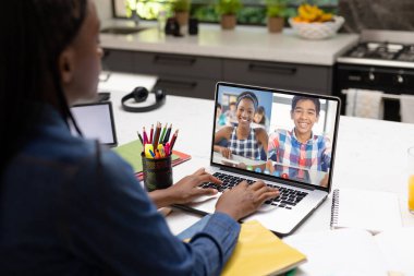 İki farklı öğrenciyle bilgisayar başında video konferansı yapan Afro-Amerikan bayan öğretmen. Uzak öğrenim çevrimiçi eğitim kavramı