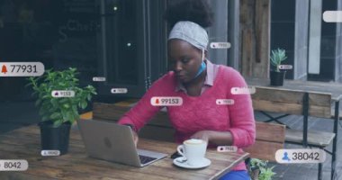 Bir kafede dizüstü bilgisayar kullanan Afrikalı Amerikalı bir kadının sosyal medya simgelerinin animasyonu. Sosyal medya ağı ve covid-19 salgın konsepti
