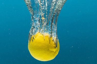 Mavi arkaplanda kopya alanı olan limonun suya düşüşünü kapat. Meyve, vejetaryen yemeği ve renk konsepti.