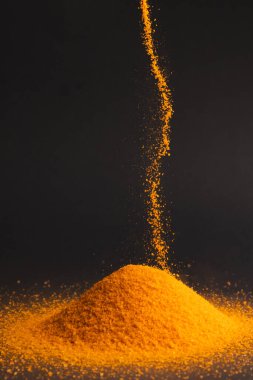 Turuncu kum yığınına dökülen ve siyah arkaplana boşluğu kopyalayan. Kum, doku, hareket, şekil ve renk kavramı.