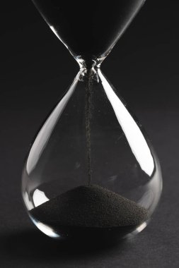 Kum saatini siyah kumla kapat ve siyah arkaplana kopyala. Zaman, zaman tutma, şekil ve renk kavramı.