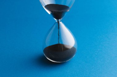 Kum saatini siyah kumla kapat ve mavi arkaplanda kopyala. Zaman, zaman tutma, şekil ve renk kavramı.