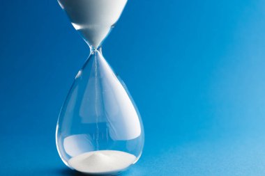 Close up of hourglass with white sand and copy space on blue background. Time, timekeeping, shape and colour concept. clipart