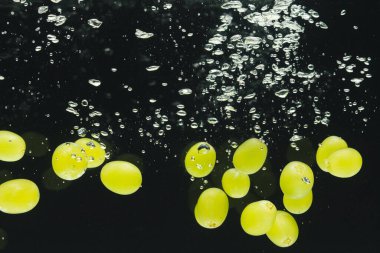 Siyah arka planda kopya alanı olan beyaz üzümlerin suya düşüşünü kapat. Meyve, vejetaryen yemeği ve renk konsepti.