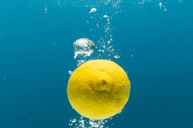 Mavi arkaplanda kopya alanı olan limonun suya düşüşünü kapat. Meyve, vejetaryen yemeği ve renk konsepti.