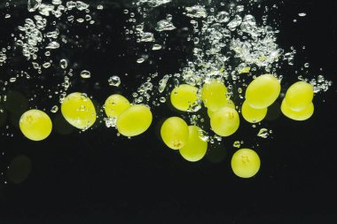 Siyah arka planda kopya alanı olan beyaz üzümlerin suya düşüşünü kapat. Meyve, vejetaryen yemeği ve renk konsepti.