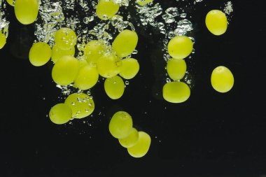 Siyah arka planda kopya alanı olan beyaz üzümlerin suya düşüşünü kapat. Meyve, vejetaryen yemeği ve renk konsepti.