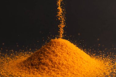 Turuncu kum yığınına dökülen ve siyah arkaplana boşluğu kopyalayan. Kum, doku, hareket, şekil ve renk kavramı.