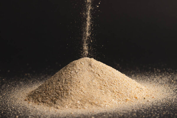 Close up of sand pouring into heap and copy space on black background. Sand, texture, movement, shape and colour concept.