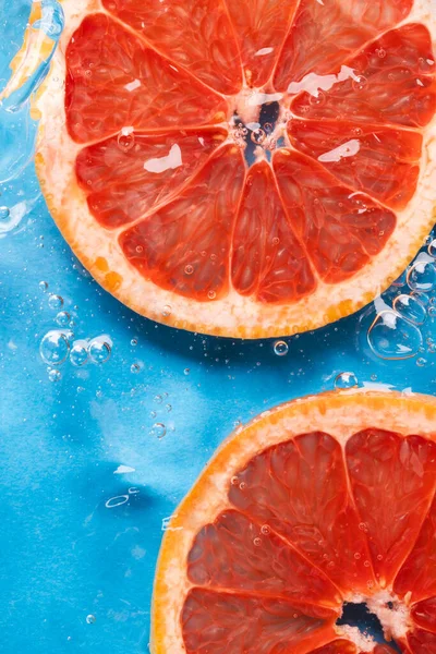 Close up of red grapefruit slices in water with copy space on blue background. Fruit, vegan food and colour concept.
