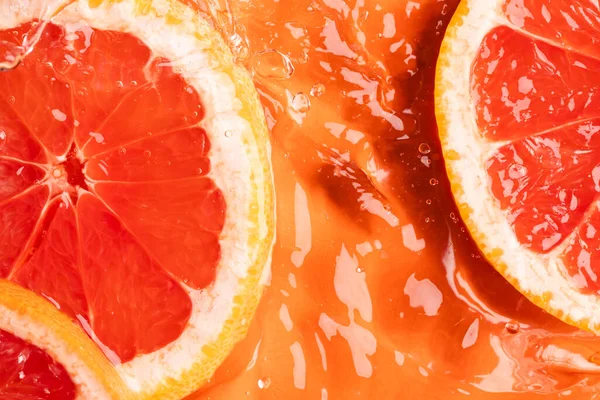 Close up of red grapefruit slices in water with copy space on orange background. Fruit, vegan food and colour concept.