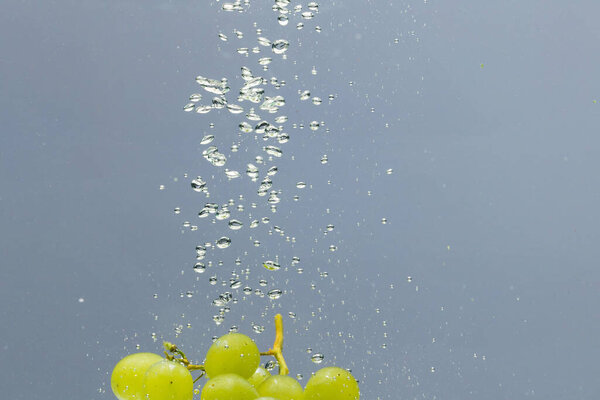 Close up of white grapes falling into water with copy space on grey background. Fruit, vegan food and colour concept.