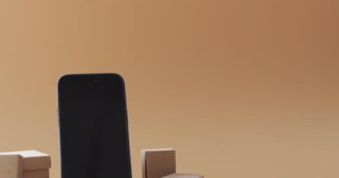 Boş ekranlı akıllı telefon videosu ve turuncu arka planda fotokopi alanı olan kutular. Siber alışveriş, çevrimiçi alışveriş, gemicilik, teknoloji ve küresel bağlantılar kavramı.