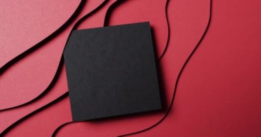 Dalgaların kesilmesi ve kırmızı arkaplanda boşluğun kopyalanması üzerine siyah kağıdın karesinin yakın çekim videosu. Kağıt, kırtasiye, şekil ve renk kavramı.