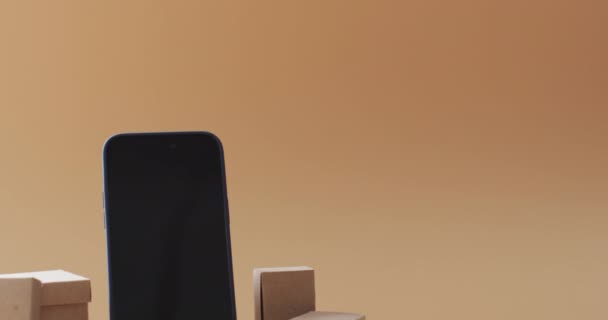 オレンジ色の背景にコピースペースのある空白の画面とボックスを備えたスマートフォンのビデオ サイバーショッピング オンラインショッピング テクノロジー グローバルコネクションのコンセプト — ストック動画
