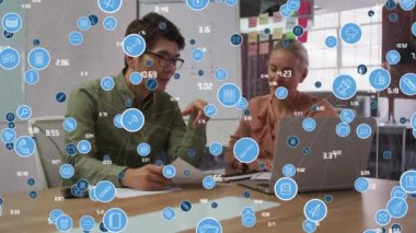 Animation of network of digital icons over diverse man and woman discussing at office. Global networking and business technology concept