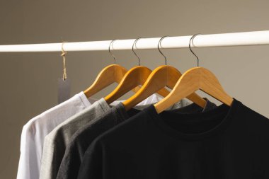 Elbise korkuluklarından sarkan dört tişört ve gri arka planda fotokopi alanı. Moda, kıyafetler, renk ve kumaş konsepti.